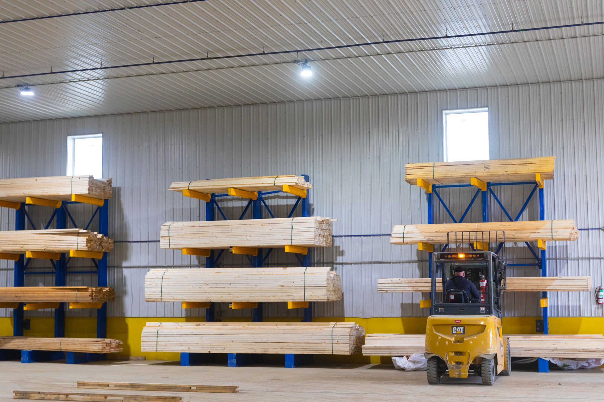 Lumber stored on cantilever racks with a forklift moving stock.