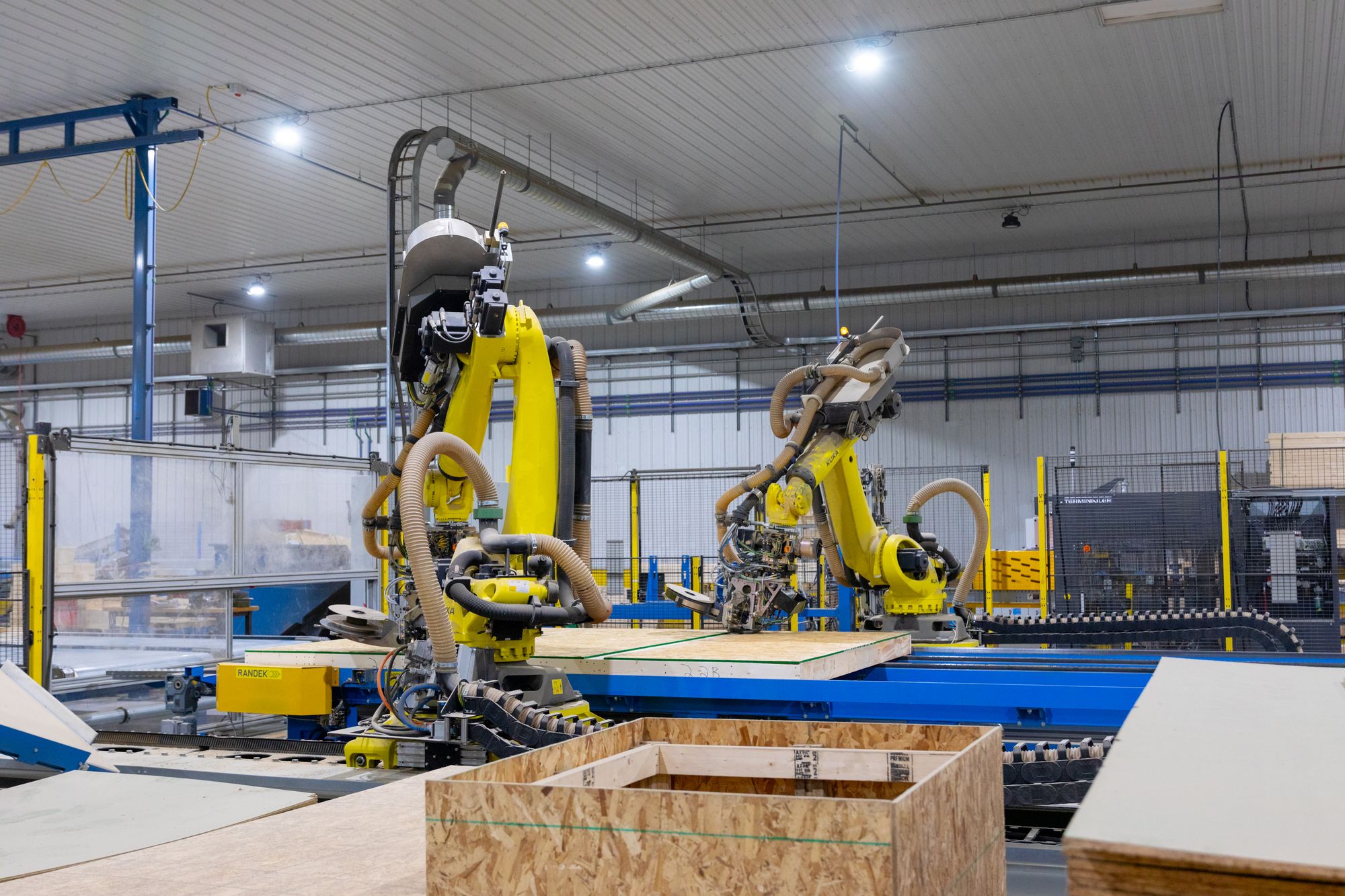 Two robotic arms working on a sheathed wall panel on the panel line.